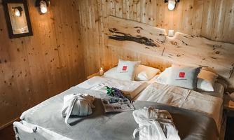 A cozy room with wooden paneling and two beds. On the bed are towels and a small table with a magazine.