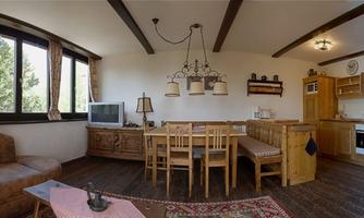 A cozy kitchen and living area with a large wooden dining table and a comfortable couch. The large windows let in plenty of light and provide a view of the outdoors.