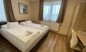 A simple room with two single beds and a desk. The sunlight shines through the windows, creating a friendly atmosphere.