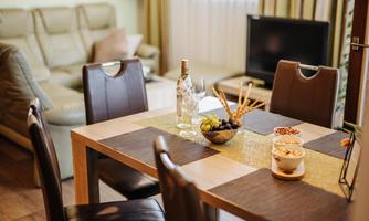 A cozy dining area with a table that has snacks and drinks on it. In the background, a living room and a television can be seen.