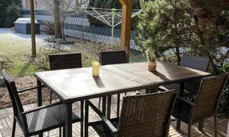 A cozy outdoor area with a wooden table and chairs. Surrounded by plants and featuring a covered terrace.