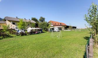 A tranquil rural scene with a green garden and a small soccer goal. In the background, several houses and trees are visible.