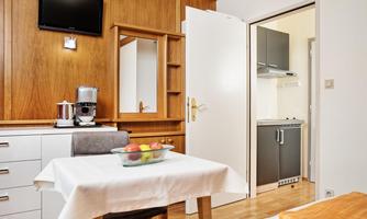 A modern room with a table, chairs, and a fruit bowl. The kitchen is visible in the background, with elegant wood and metal accents.