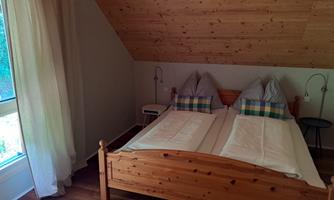 A cozy bedroom with a wooden bed and two pillows. The room has large windows and is decorated with wooden paneling.
