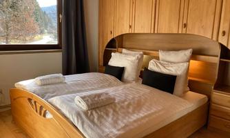 A cozy bedroom with a wooden double bed and two large windows. Soft bed linens and towels are ready to create a relaxing atmosphere.