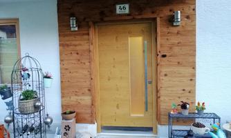 An inviting wooden front door with a modern design. Next to it are decorative plants and a stylish plant table.