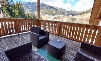 A cozy balcony with rattan furniture that offers a view of the mountains and the surrounding nature. The sky is partly cloudy, and there is a relaxed atmosphere.