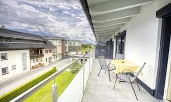A balcony with a table and chairs that offers a view of the surrounding buildings. The sky is cloudy and there is a calm atmosphere.