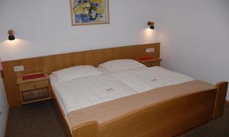A cozy bedroom with a double bed and warm wood tones. There are some pictures hanging on the walls and there is warm lighting.
