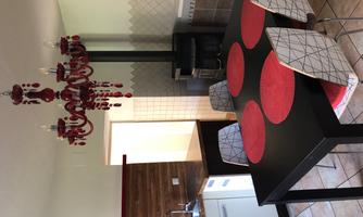 A modern kitchen with a black dining table and red placemats. Above the table hangs a red chandelier.