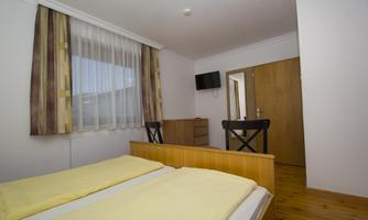A simple bedroom with two single beds and a television. The walls are light and there is a wooden floor.