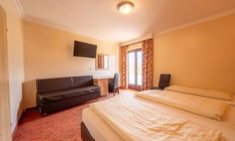 A simple room with two single beds and a television on the wall. There is a sofa and a small table as well as windows with curtains.