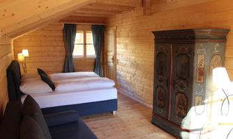 A cozy room with wooden walls and a double bed. Next to the bed, there is a sofa and an old wardrobe.