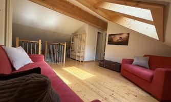 A cozy room with red sofas and a wooden floor. Bright beams of light fall through the skylights, creating an inviting atmosphere.