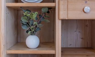 A cozy wooden shelf with a clock, a small plant in a white vase, and a framed document. The accents of white buttons give the shelf a special charm.
