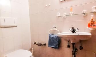 A small bathroom with white tiles. There is a sink, a toilet, and a mirror on the wall.