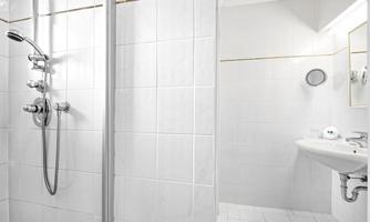 A modern bathroom with a shower and a sink. The walls are finished in light tiles, and it is well-lit.
