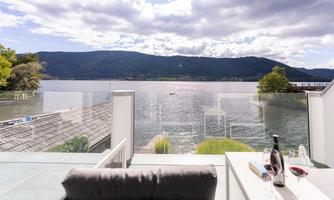 A peaceful lake landscape with mountains in the background. In the foreground, a cozy seating area and a bottle of wine on a table.