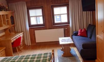 A cozy room with two beds, a sofa, and a desk. Pine wood walls and wooden ceilings give the space a warm atmosphere.