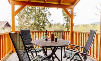 A cozy balcony with a round table and black chairs. In the background, trees and a green landscape can be seen.