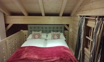 A cozy bedroom with a large bed and red blankets. The walls are made of light wood, and there are decorative pillows.