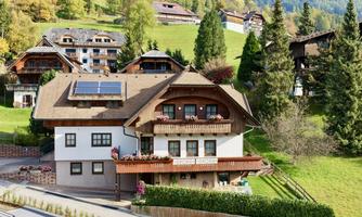 A charming house with a wooden balcony and blooming plants. Surrounded by green meadows and mountains in the background.