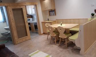 A cozy dining area with a wooden table and chairs. In the background, a modern kitchen and a bathroom are visible.