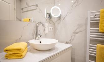 A modern bathroom with a sink and a large mirror. Yellow towels are neatly placed on a white dresser.