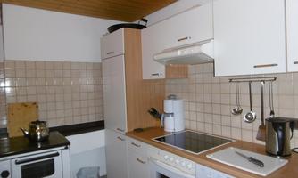 A modern kitchen with a bright wooden ceiling. It includes a stove, a refrigerator, and various kitchen appliances on a bright countertop.
