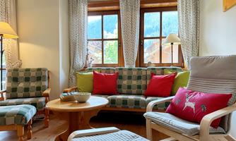 A cozy living room with two windows and a view of the mountains. Comfortable furniture and colorful cushions create an inviting atmosphere.