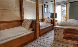 A cozy bedroom with wooden beds and a warm atmosphere. The room has a window overlooking the outside and a sturdy table.