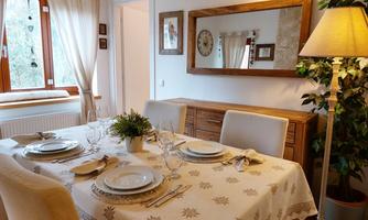 An inviting dining area with a beautifully set table and a lovely tablecloth. The light gently falls through the windows, creating a cozy atmosphere.