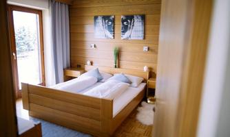 A modern bedroom with wooden paneling and a double bed. Pictures hang on the walls and a large window allows for plenty of daylight.