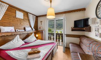 A cozy bedroom with a double bed and wooden paneling. Large windows offer a view of the nature outside.