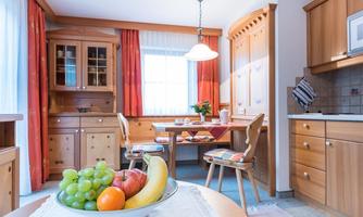 A cozy kitchen with wooden cabinets and a dining table. On the table, there is a bowl of fresh fruit.