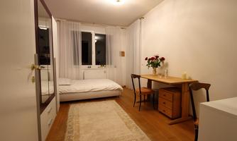 A simple bedroom with a bed, a table, and a chair. The walls are bright and there is a carpet on the floor.