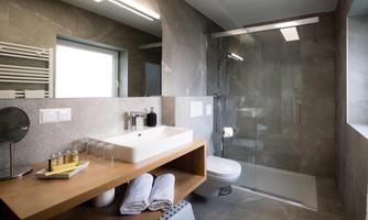 A modern bathroom with a glass shower and a stylish stone wall. On the wooden shelf are towels and toiletries.