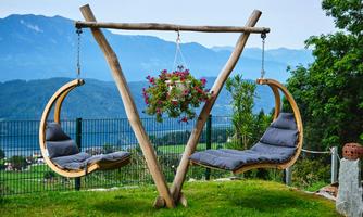 Two hanging chairs made of wood in a picturesque landscape. In the background, mountains and trees can be seen.