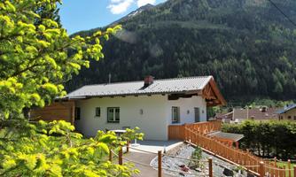 A modern house in a picturesque mountain village. In the background, green mountains and a blue sky can be seen.