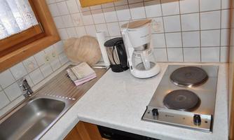 A small kitchen with a sink, a coffee machine, and a stovetop. The walls are tiled with white tiles.