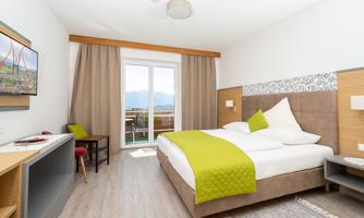 A modern bedroom with a large double bed and a bright, friendly design. The balcony door offers a beautiful view of the mountains.