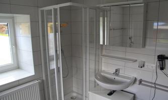 A modern bathroom with a shower and a sink. Large windows provide plenty of natural light.