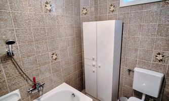A small bathroom with a bathtub, a toilet, and a white cabinet. The walls are decorated with light tiled patterns.