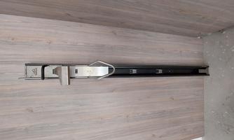 A modern stainless steel tool on a wooden surface. It looks like a measuring device or a holder.