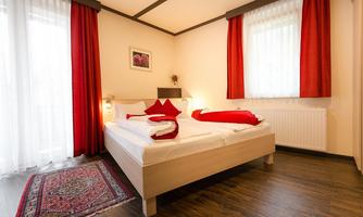 A cozy bedroom with a double bed and red curtains. The wooden floor and the carpet give the room a warm atmosphere.