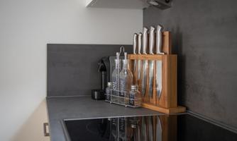 A modern kitchen with an elegant countertop.  
On the table, there is a knife set in a wooden block and some glass bottles.