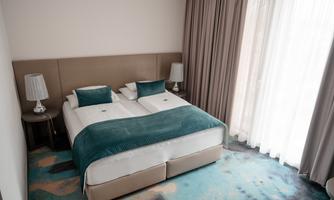 A modern bedroom with a double bed and gentle green accents. Large windows let in plenty of light and create an inviting atmosphere.