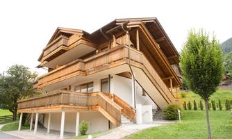 A modern wooden house with several balconies and a large garden. The surroundings are green and invite relaxation.