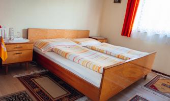 A cozy bedroom with a wooden bed and striped bedding. The room has a warm hue and large windows with red curtains.