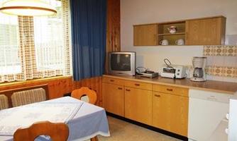 A bright kitchen with a table and chairs. Various kitchen appliances are on the countertop, while the windows let in plenty of natural light.